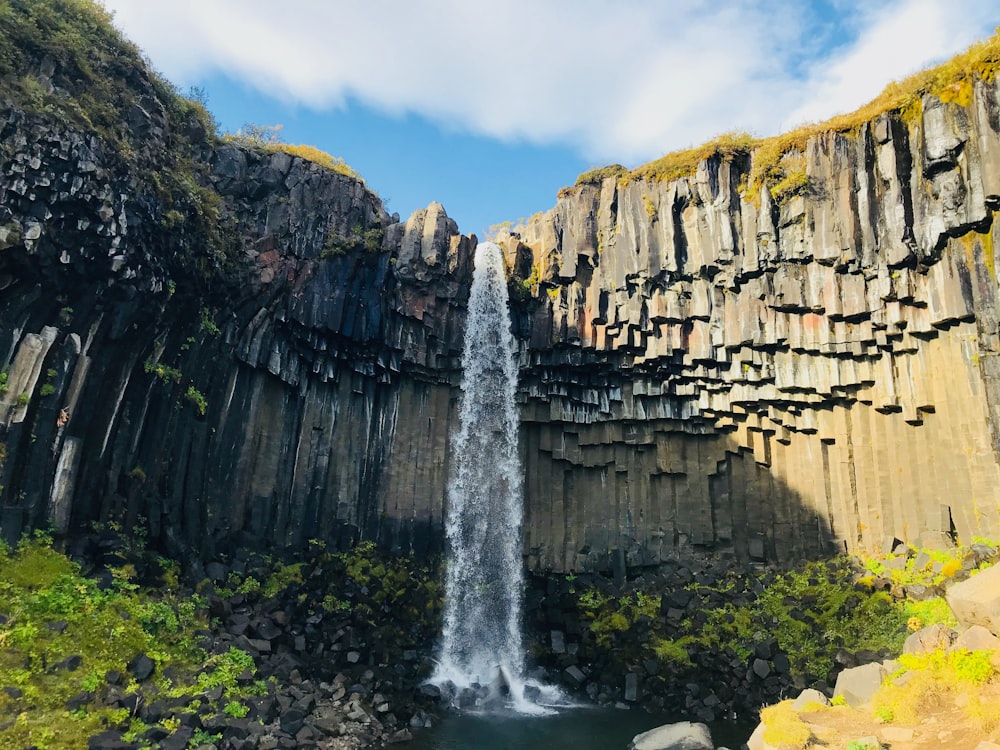 waterfalls between brown rocky mountain under blue sky during daytime