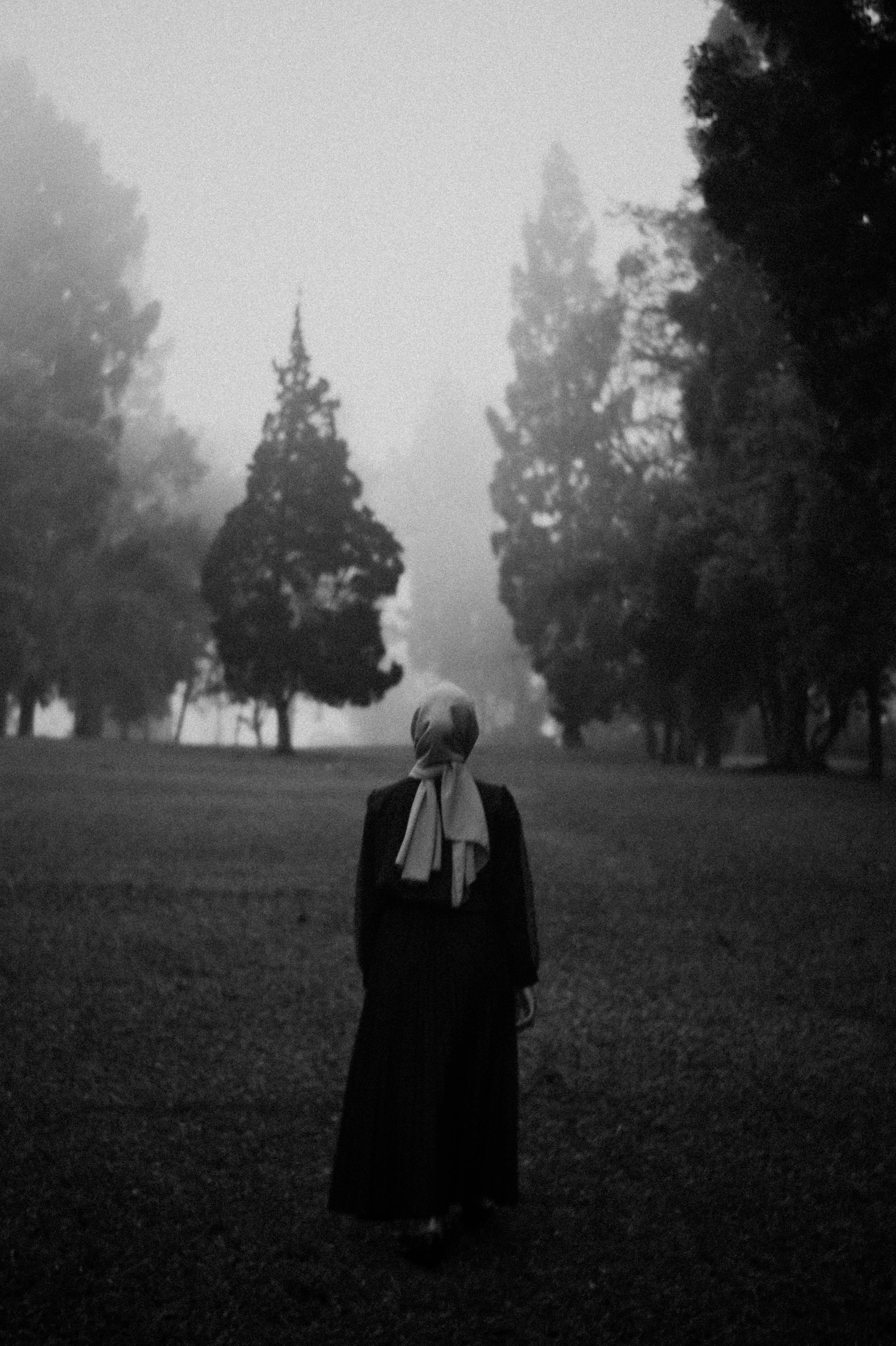 grayscale photo of woman in black dress standing on grass field