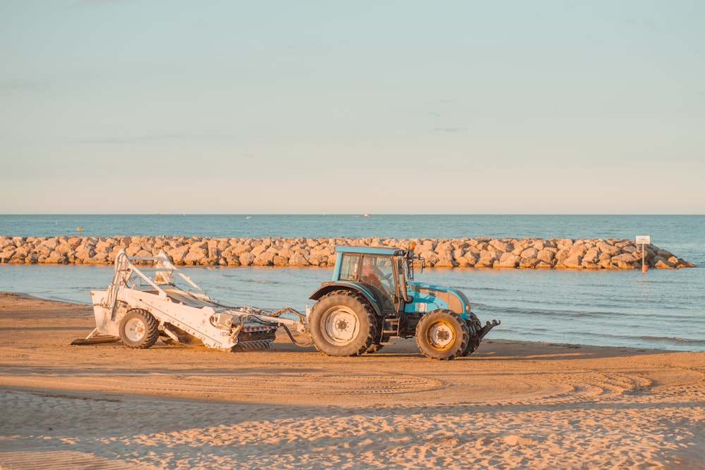 blue tractor on brown sand near body of water during daytime