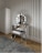 A stylish vanity area featuring a reflective, mirrored dressing table with a round mirror framed by round lights. In front of the table is a padded stool with a tufted design. The room includes a striped wallpaper, a soft gray rug, and light wood flooring.