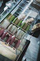 A display of delicate macarons in soft pinks and greens arranged neatly in a glass case.