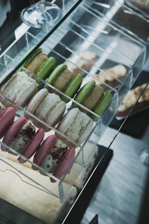 A display of delicate macarons in soft pinks and greens arranged neatly in a glass case.
