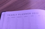A close-up view of a yearly planner for 2022, featuring months and days organized in a tabular format. The planner is open on a wooden surface and has a soft purple tint.