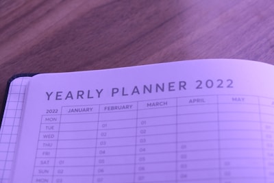 A close-up view of a yearly planner for 2022, featuring months and days organized in a tabular format. The planner is open on a wooden surface and has a soft purple tint.