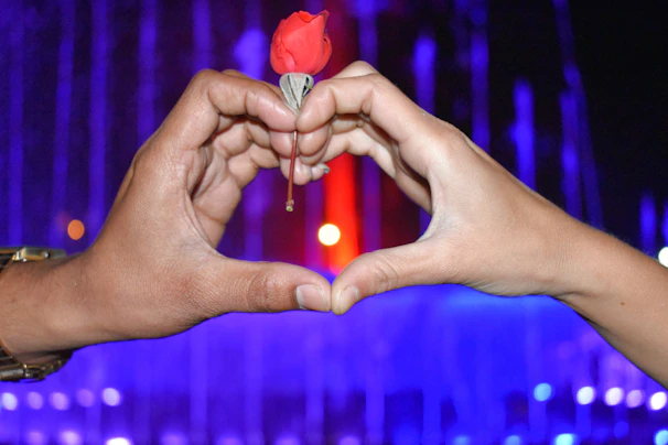 Close-up of hands casting a love spell with rose petals and a heart-shaped charm.