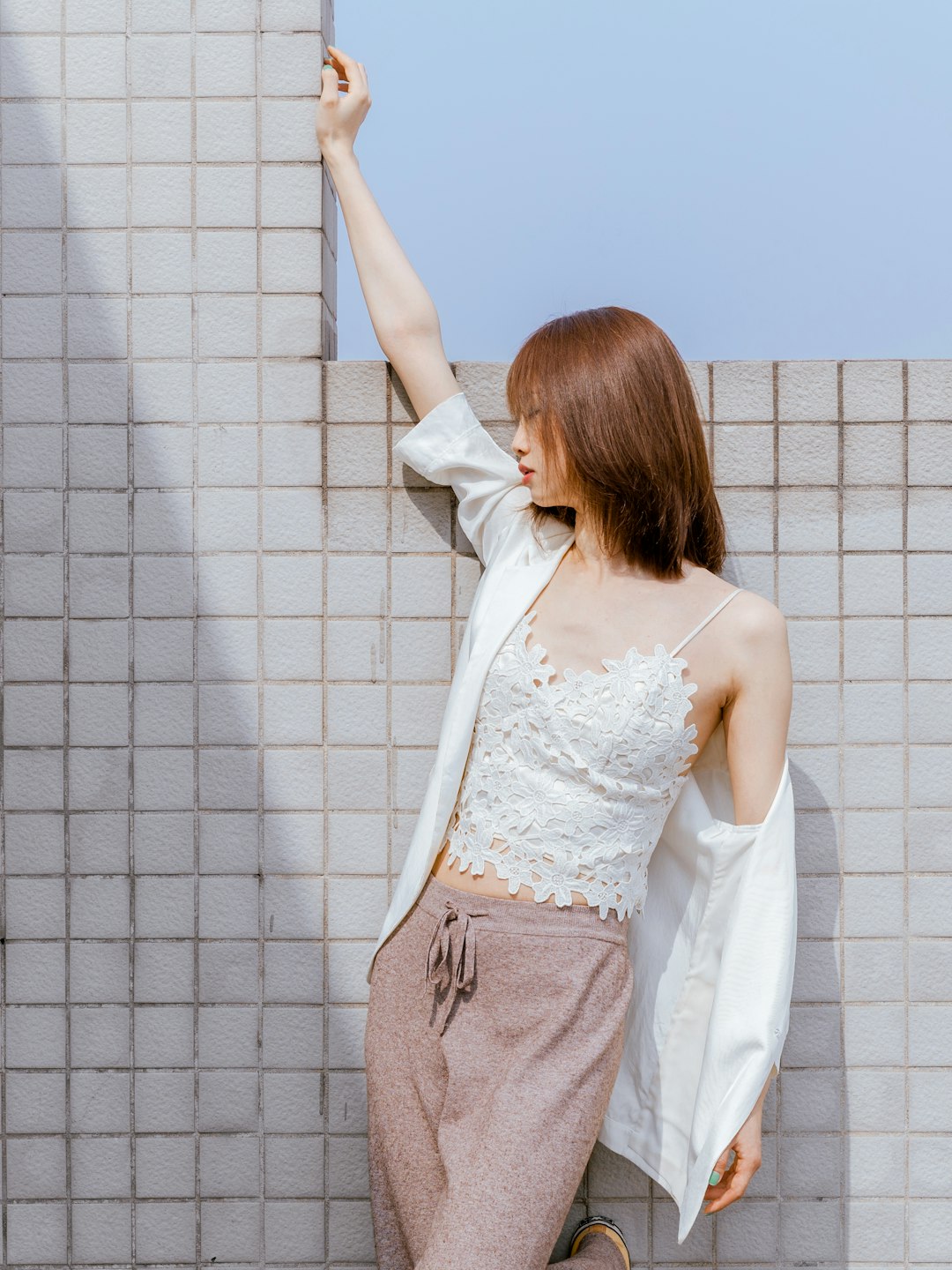 woman in white floral lace tank top and gray pants standing beside white concrete wall during