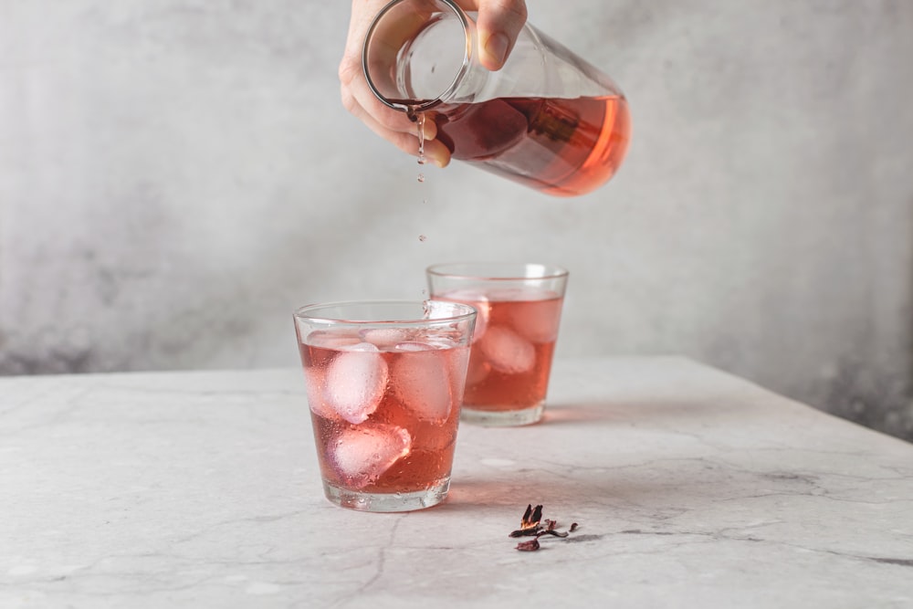 person pouring red liquid on clear drinking glass