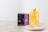 A glass filled with a refreshing beverage containing ice, lemon, and lime slices is placed on a wooden coaster beside a black and purple box labeled 'Elixir Detox AGATA' from Crystaltea. The setup is against a light, minimalist background.