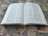 An open bilingual book featuring pages with text in both English and Korean. It is placed on a colorful, patterned fabric surface, possibly a tapestry or carpet.