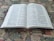 An open bilingual book featuring pages with text in both English and Korean. It is placed on a colorful, patterned fabric surface, possibly a tapestry or carpet.