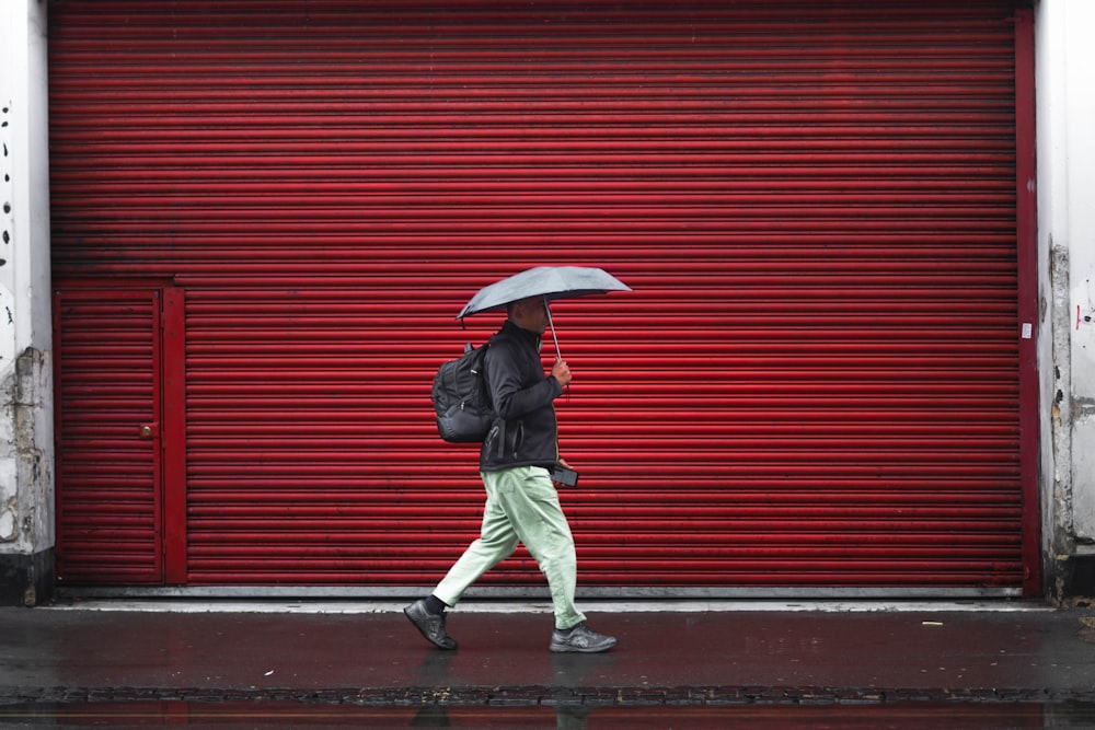검은 재킷과 회색 바지를 입은 남자가 우산을 들고 보도를 걷고 있다