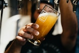 person holding clear drinking glass with yellow liquid