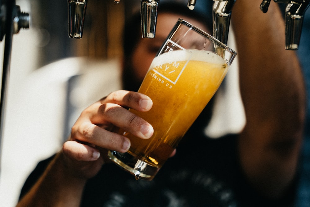 person holding clear drinking glass with yellow liquid