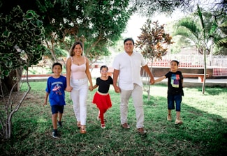 A diverse group of people standing hand in hand in a green park, smiling warmly at each other.