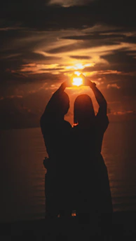 Silhouettes of a couple holding hands under a shower of heart-shaped confetti.