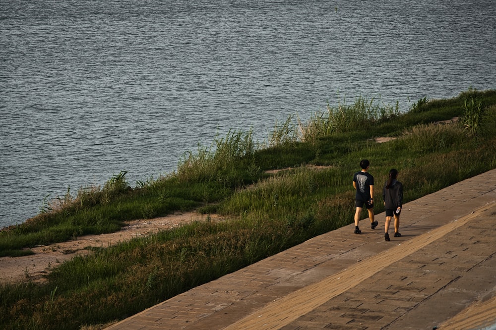 man and woman walking on pathway near body of water during daytime