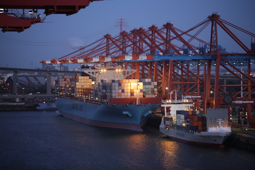 A busy port with cranes unloading containers onto trucks at sunset.