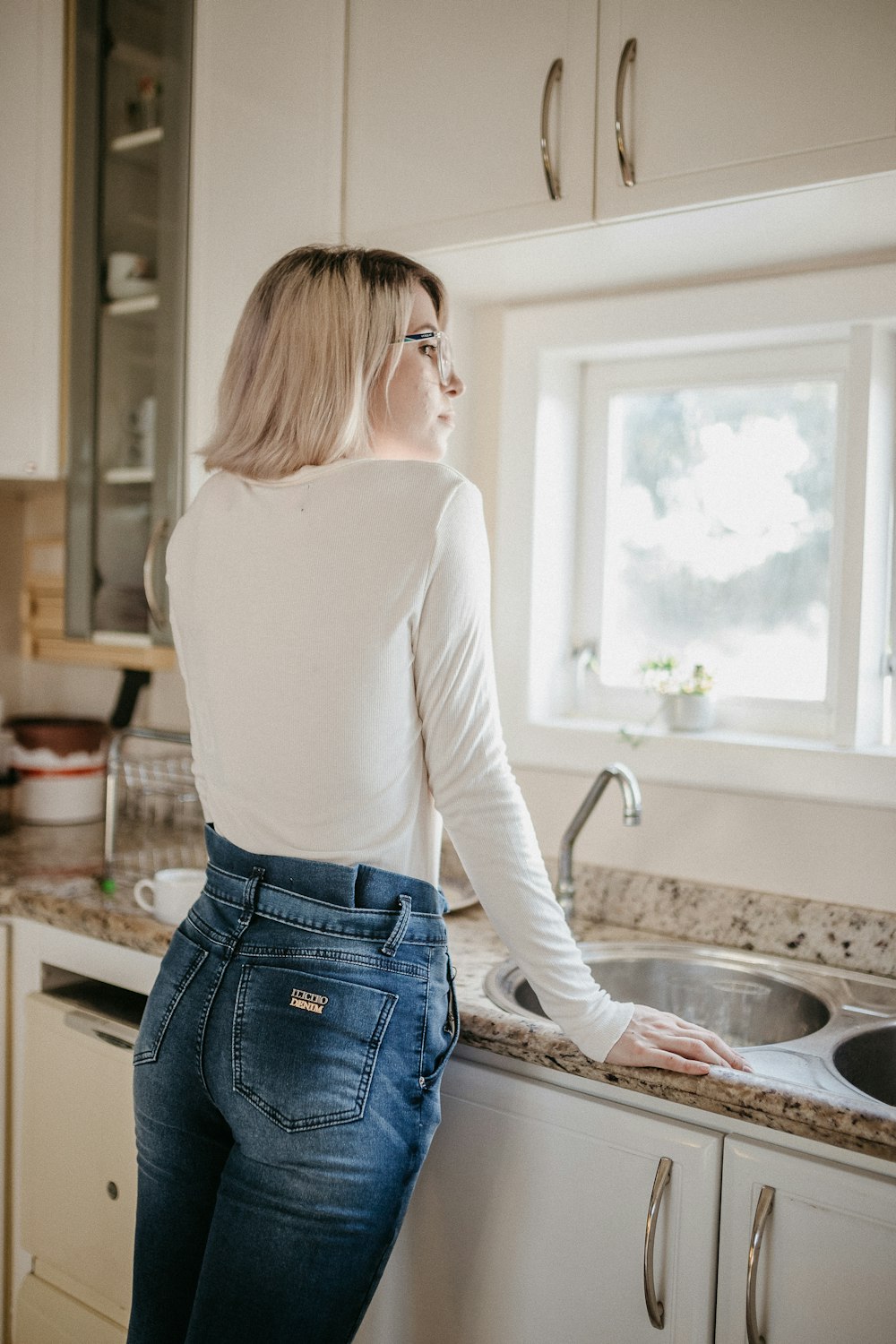 woman in white long sleeve shirt and blue denim jeans standing in front of sink