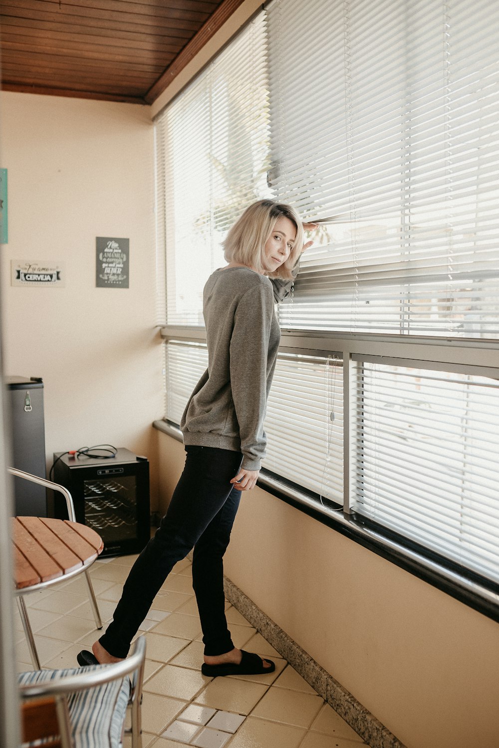 woman in gray long sleeve shirt and black pants standing near window