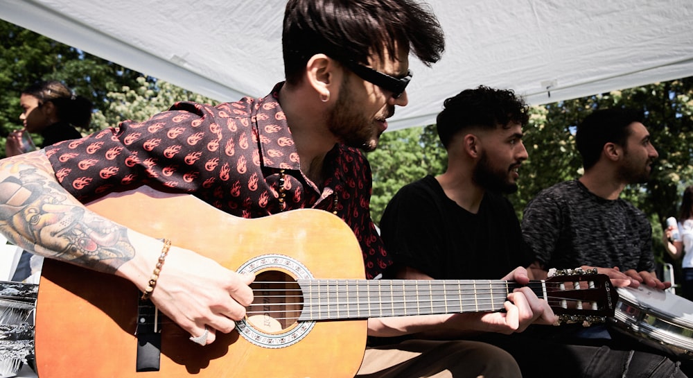 man in black and red floral button up shirt playing acoustic guitar