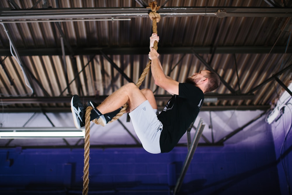 man in black t-shirt and black shorts sitting on brown rope