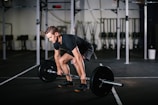 man in black t-shirt and black shorts holding black barbell