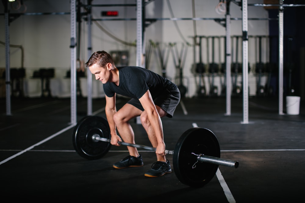 man in black t-shirt and black shorts holding black barbell
