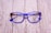 A pair of stylish eyeglasses with blue and brown tortoiseshell frames resting on a textured wooden surface. The lenses are clear, and the brand name 'Veltom' is visible in black on the lens surface.
