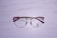 A pair of eyeglasses with a metallic gold frame and pink accents rests on a textured, white wooden surface. The lenses are clear, and there is a logo on the left lens with the word 'VELTOM'.