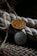Two intricately designed coins are placed against a textured background of coiled rope and woven fabric. One coin is gold-colored, while the other is silver-toned, each featuring detailed inscriptions and symbols.