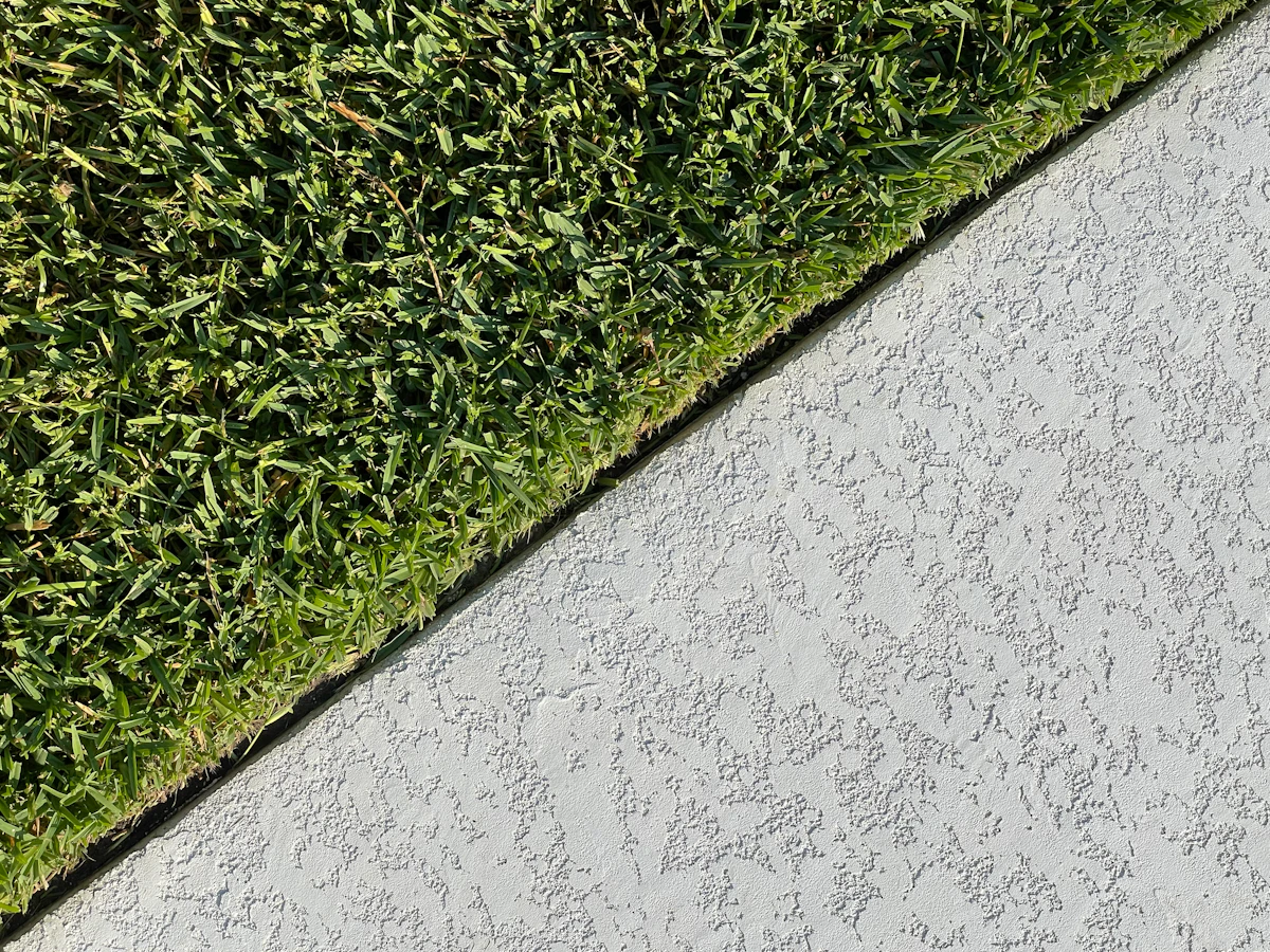 Crisp diagonal edge between manicured green lawn and textured concrete walk