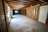 A spacious unfinished basement with exposed wooden beams on the ceiling and concrete floors. The walls are partially covered with wooden framing and plastic sheets. There is a door on the right side and a small window at the end of the room, providing some natural light. Pipes and ductwork are visible along the ceiling.