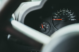A close-up view of a car dashboard featuring a speedometer and a fuel gauge, with the speedometer reading at zero and the fuel gauge indicating a low level.
