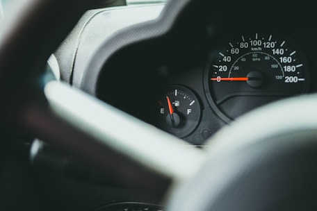 A close-up view of a car dashboard featuring a speedometer and a fuel gauge, with the speedometer reading at zero and the fuel gauge indicating a low level.