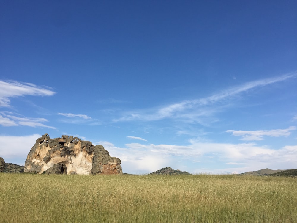 brown rock formation on green grass field under blue sky during daytime