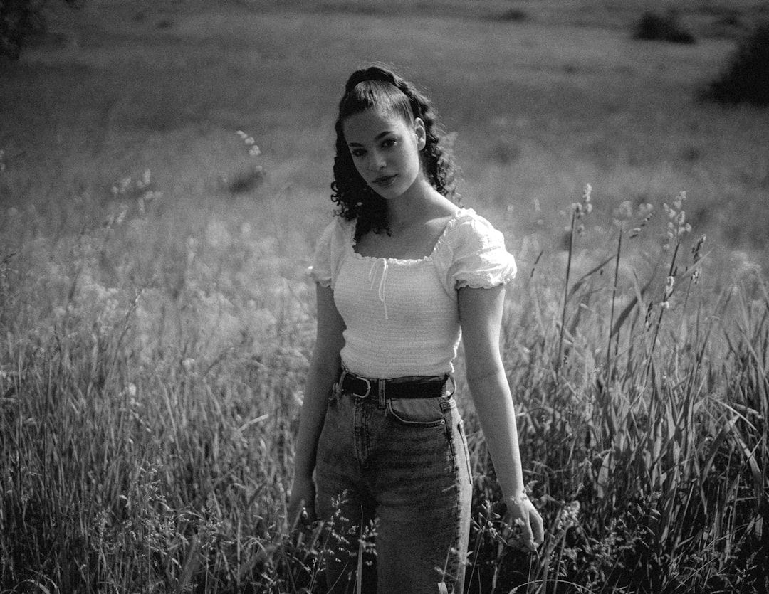 woman in white shirt and black denim jeans standing on grass field in grayscale photography