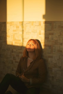 woman in black jacket sitting beside brick wall