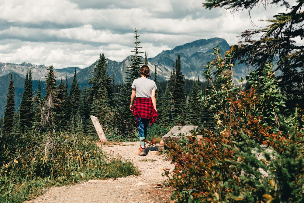 man in red shirt standing on brown rock near green trees during daytime