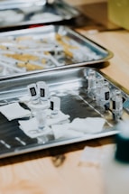 A medical setting with stainless steel trays containing multiple syringes and small vials, possibly of vaccine or medication. Gauze pads are also visible, suggesting preparedness for medical procedures.