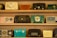 A collection of vintage radios is displayed on wooden shelves. Each radio has a distinct design and color, ranging from teal and black to yellow and red. The styles reflect a bygone era with dials, knobs, and mesh speaker coverings, showcasing the aesthetic diversity of mid-20th-century radio craftsmanship.