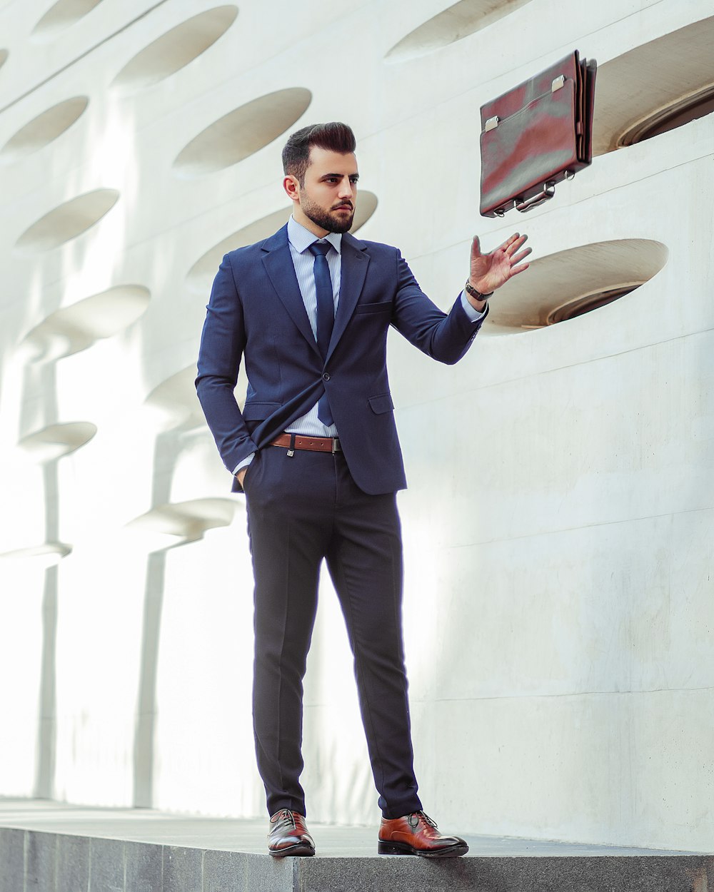 man in blue dress shirt and black pants standing near white wall