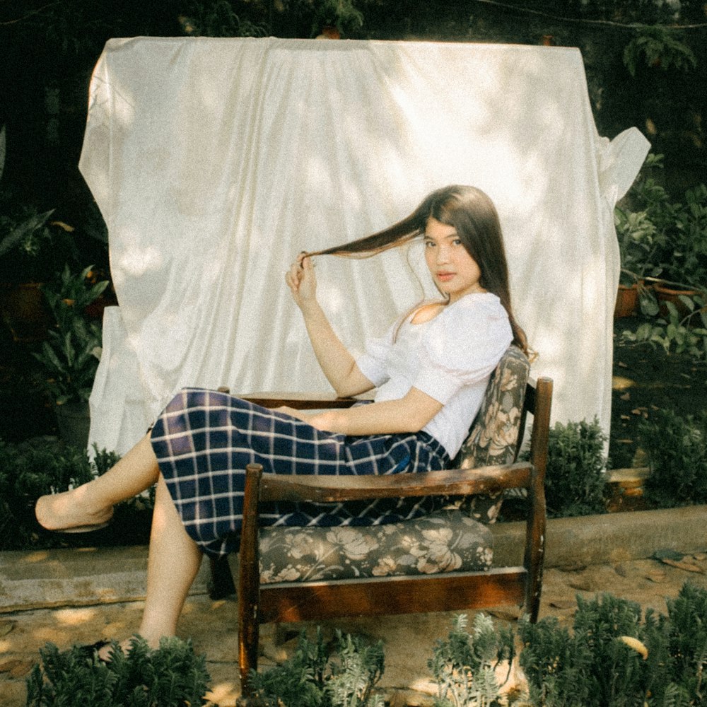 woman in white shirt and blue plaid skirt sitting on brown wooden armchair
