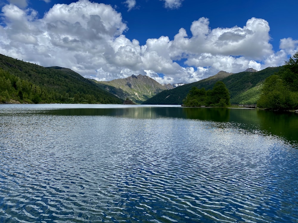 Montagnes vertes à côté du plan d’eau sous un ciel bleu et des nuages blancs pendant la journée