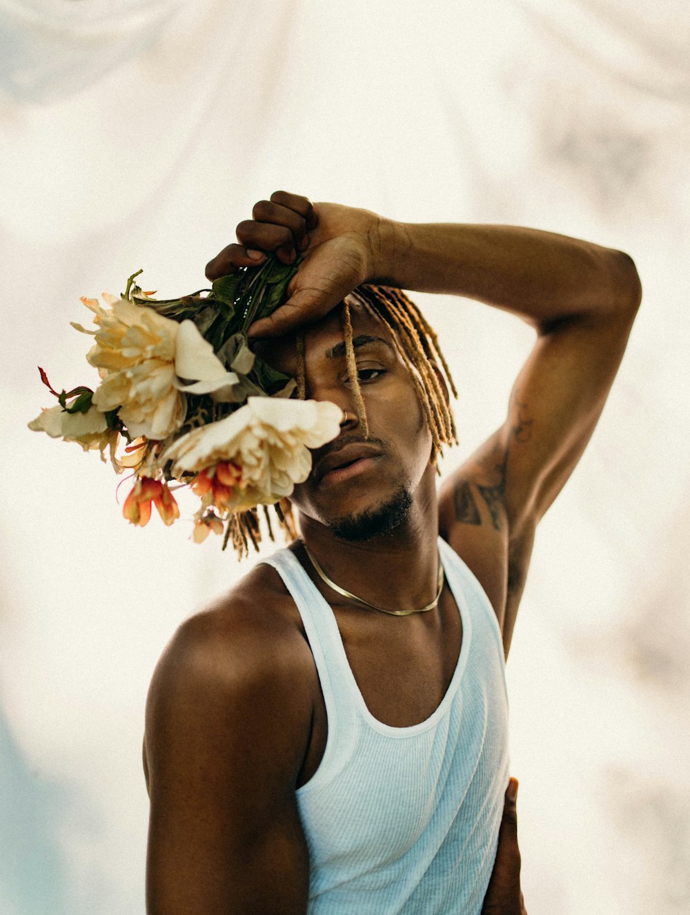 man in white tank top holding white flower