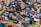A large pile of multicolored LEGO bricks and pieces is scattered across a surface. The bricks are of various shapes, sizes, and colors, including reds, blues, greens, yellows, and more. Some pieces are recognizable as wheels, windows, and other specific LEGO elements.