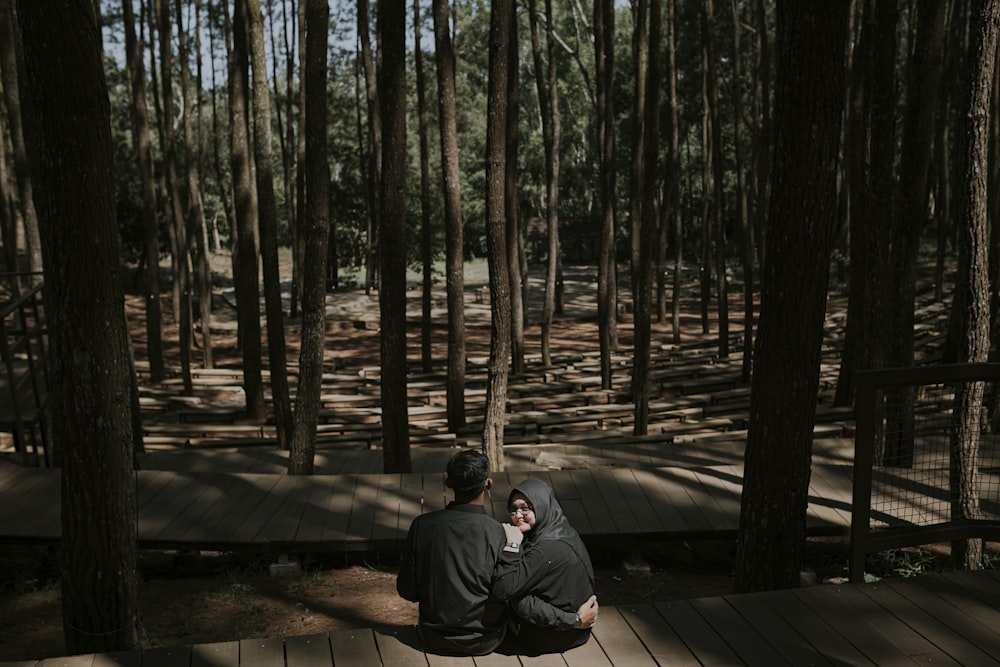 man in black jacket sitting on brown wooden dock