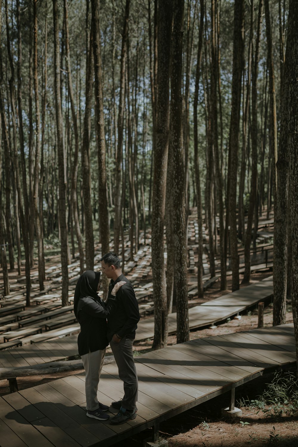 man and woman walking on wooden pathway surrounded by trees during daytime