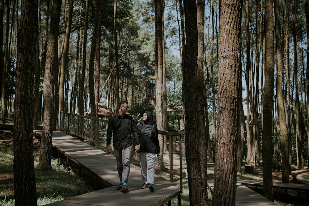 man in black jacket and black pants walking on wooden bridge