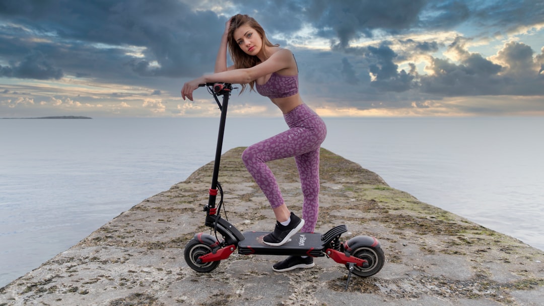 woman in pink tank top riding black and red stroller near sea during daytime