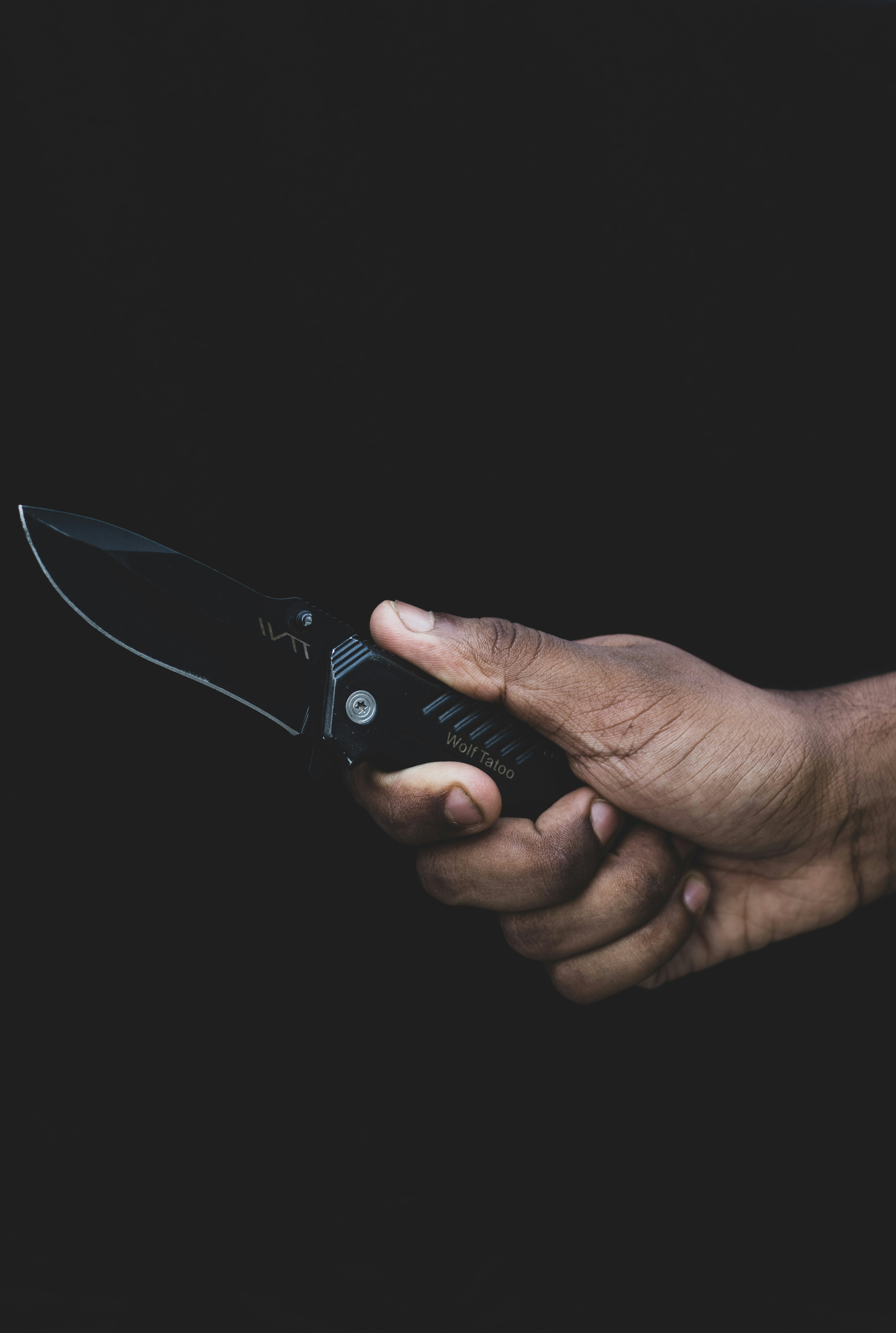 Folding military pocket knife in one hand of a boy, on a black background.